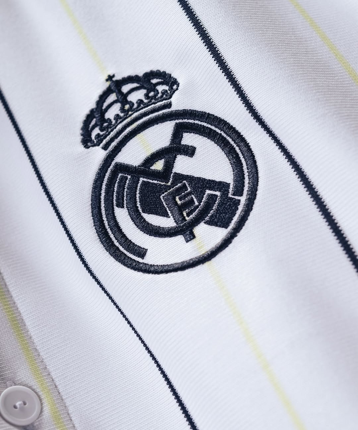 Striker Store close up of white Real Madrid special edition jersey 2025-26 with navy embroidered crest and thin yellow stripes