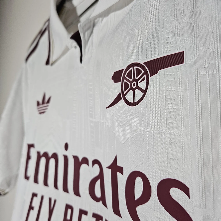 Close-up of Arsenal 2025 26 third jersey in white with burgundy cannon and Emirates Fly Better logo