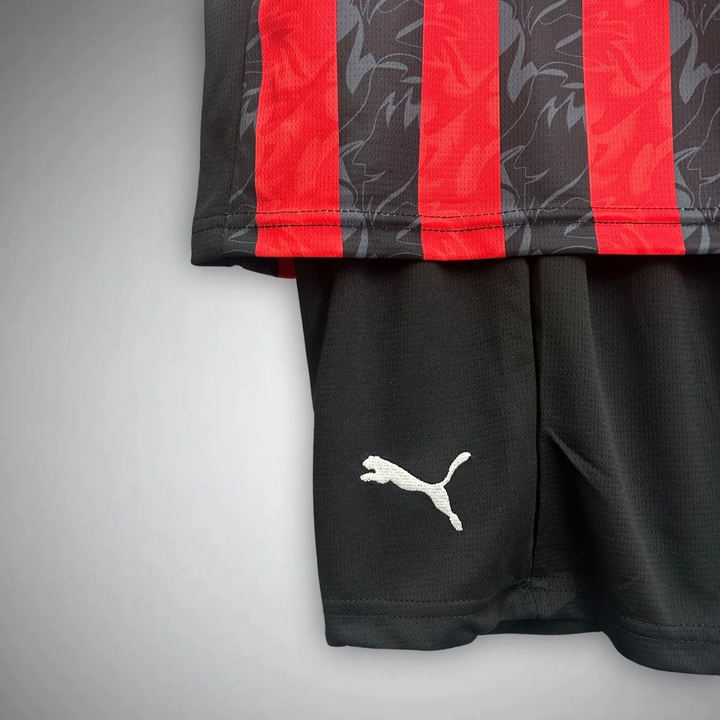 Kids AC Milan home kit 2025-26 featuring red striped jersey and black shorts by Striker Store
